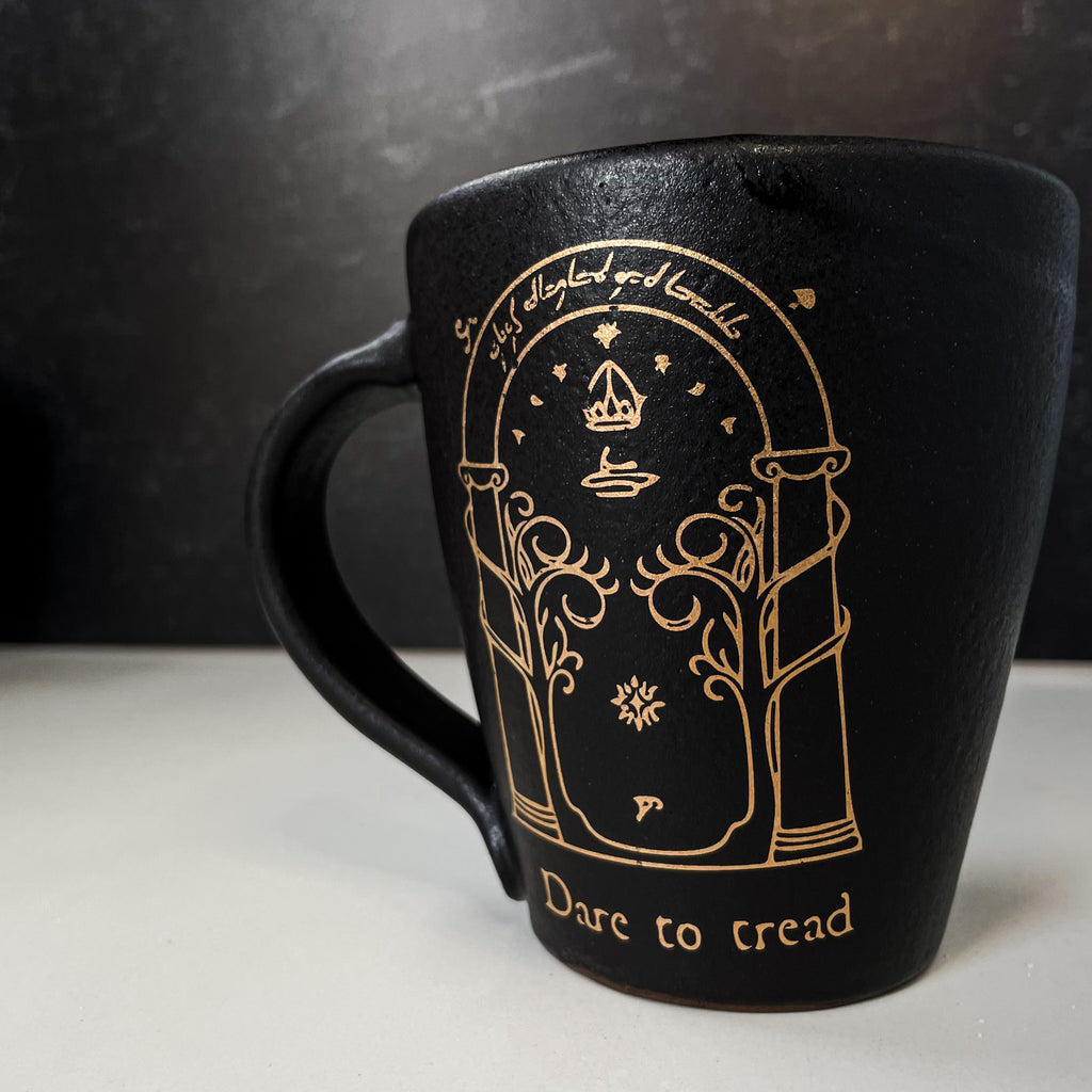 black handmade mug with 22k gold illustrated image of Durin's Door from Lord of the Rings with the words, "Dare to tread" written underneath.