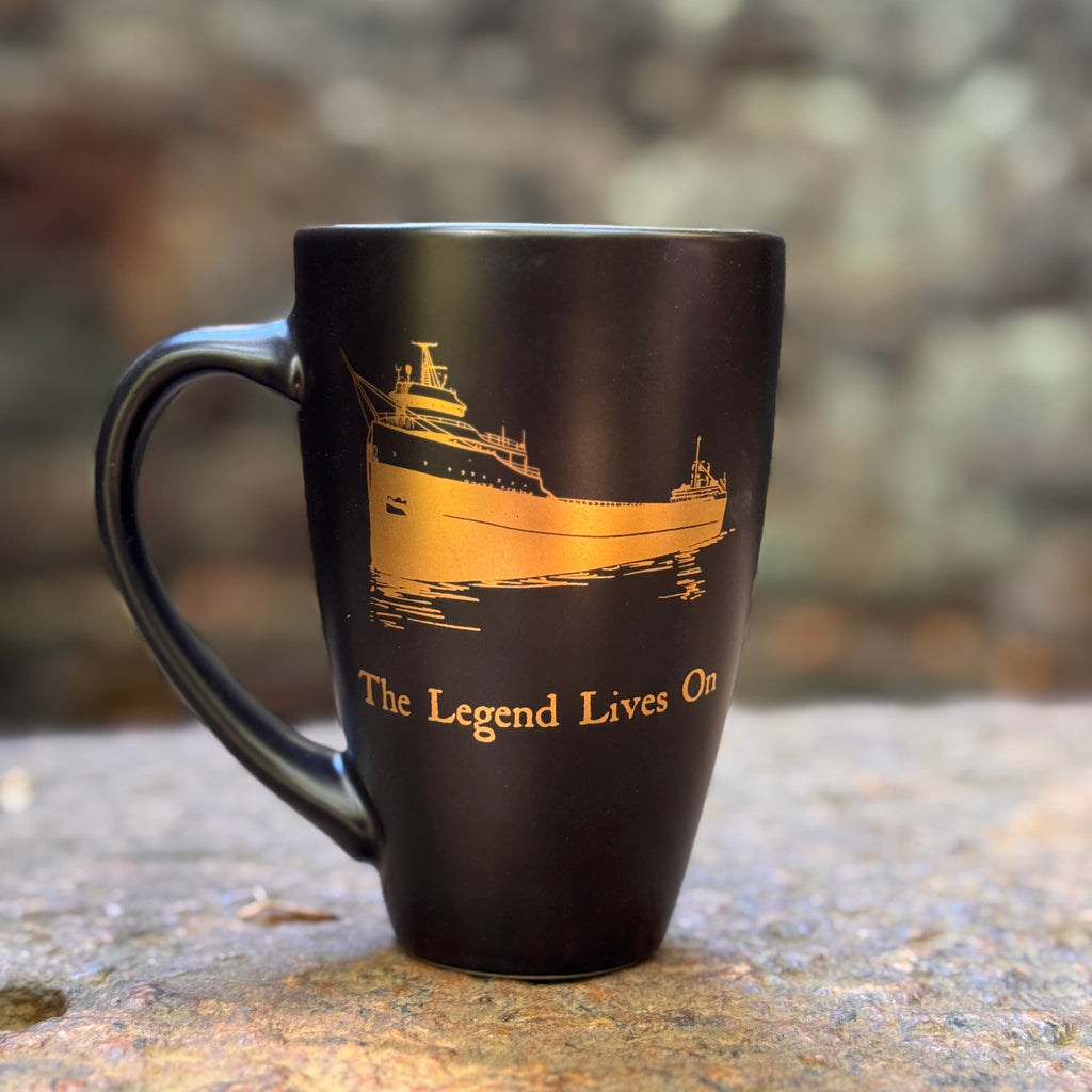 Black mug with gold ship design and 'The Legend Lives On' text on a stone surface.